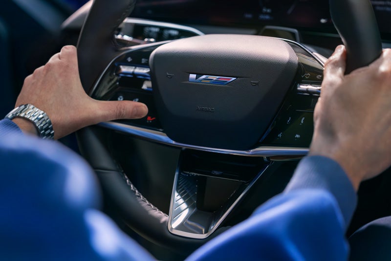 Close-up of a Man About to Press the V-Button on the 2026 OPTIQ-V Steering Wheel | McDonald Cadillac in Saginaw MI